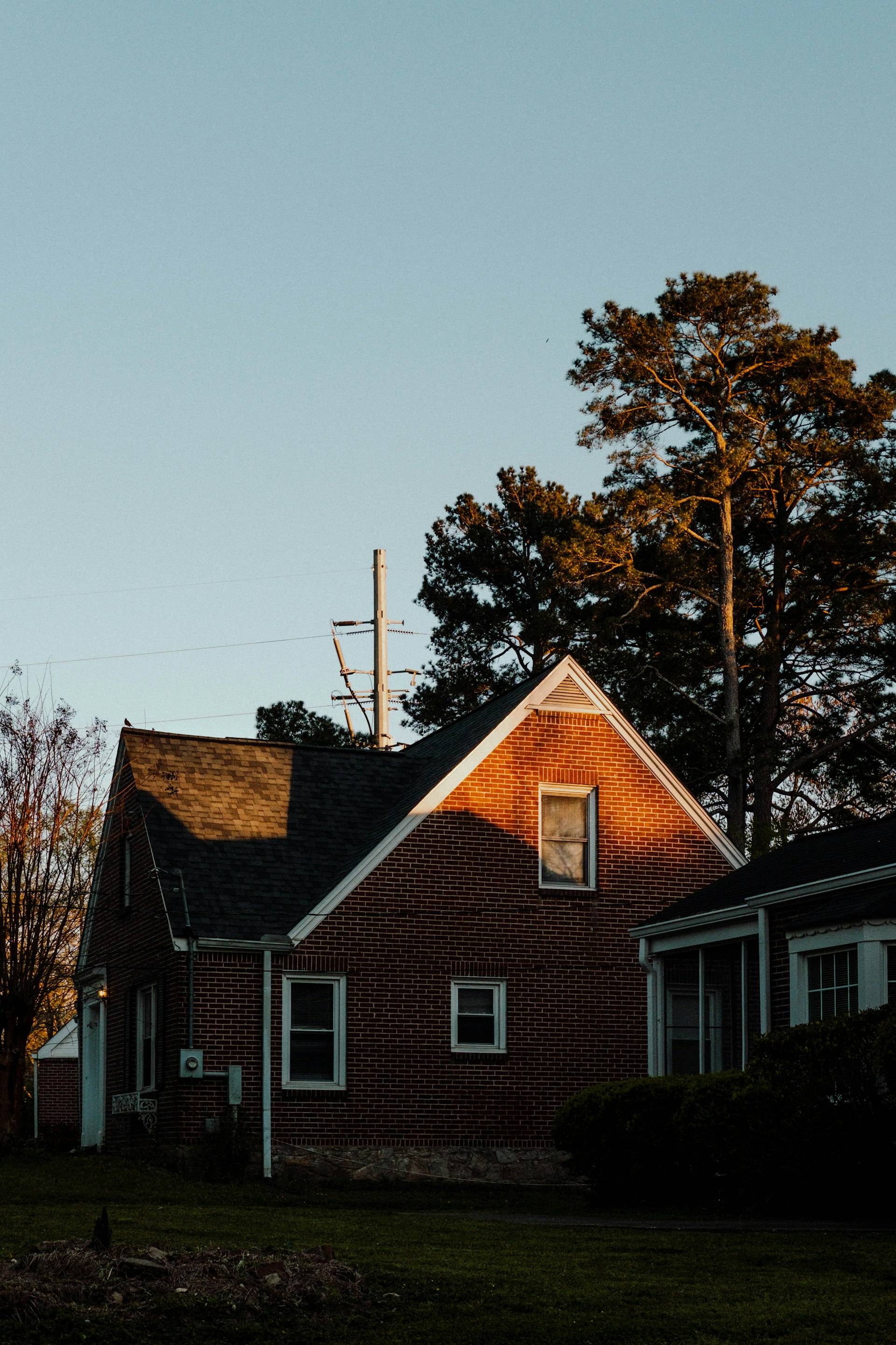 A brick house lit by golden-hour sun beneath tall pines in Atlanta