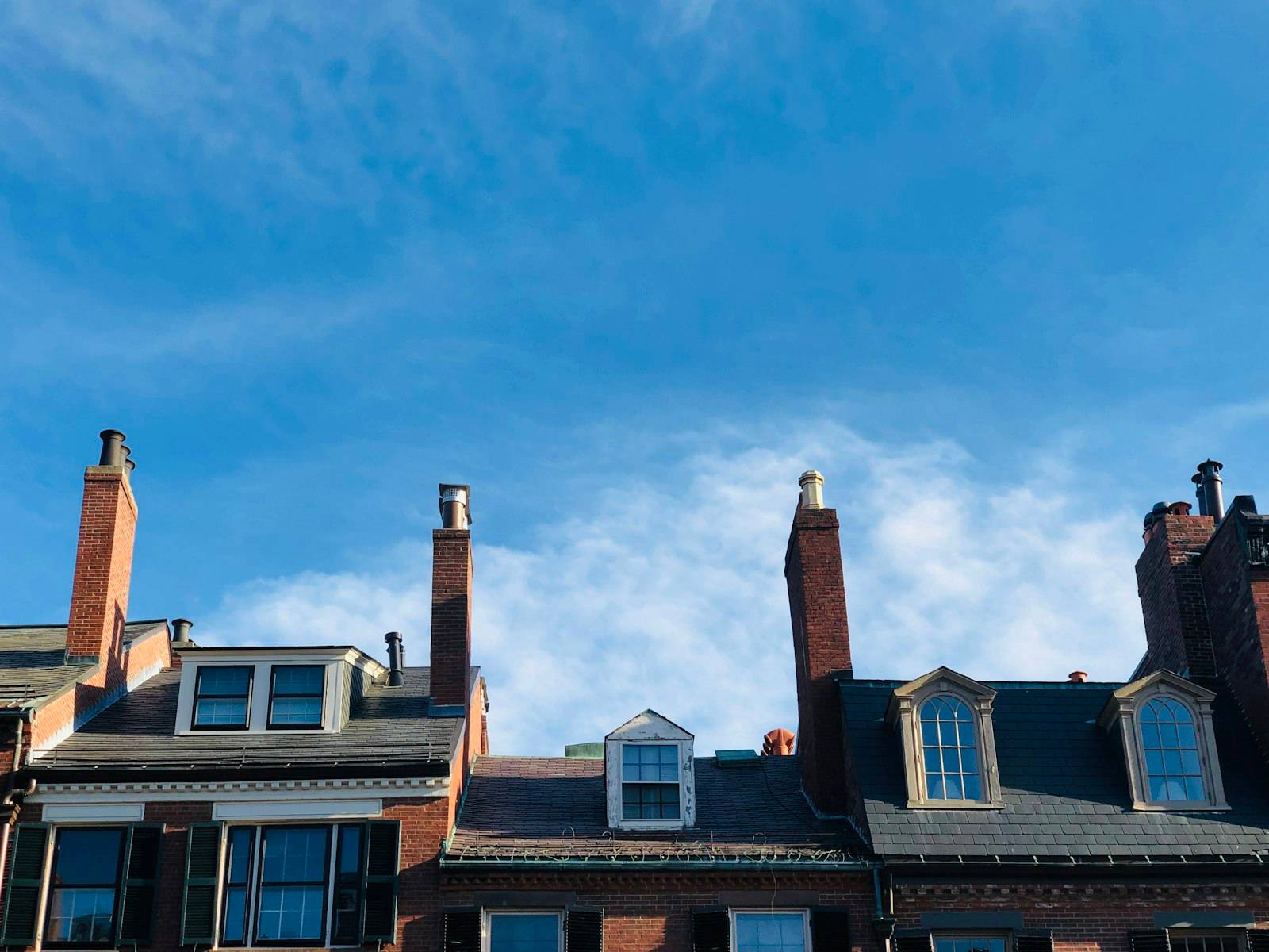 Brick Boston rowhouse rooftops with tall chimneys and dormer windows against a blue sky