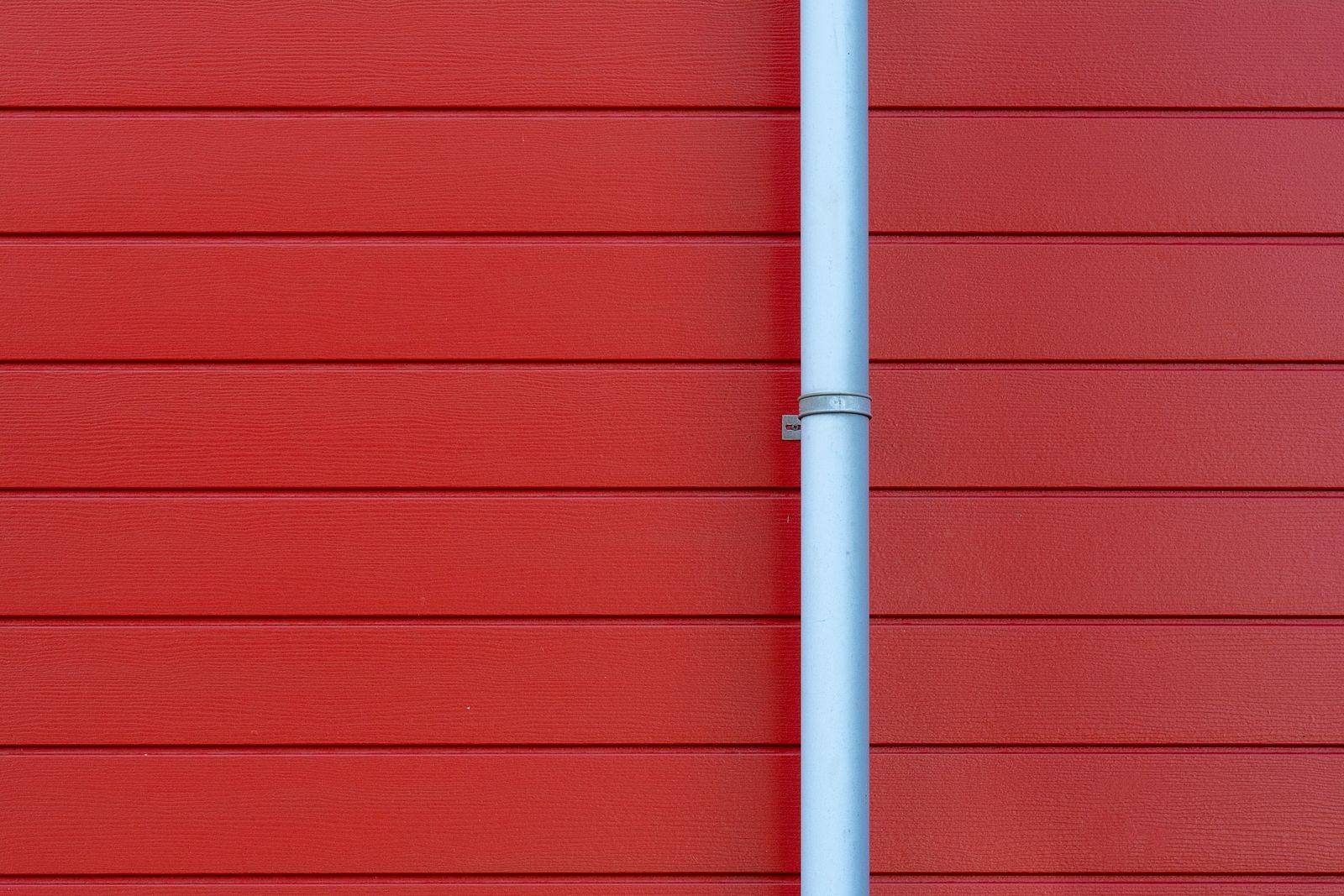 A white downspout running down a red-sided house wall