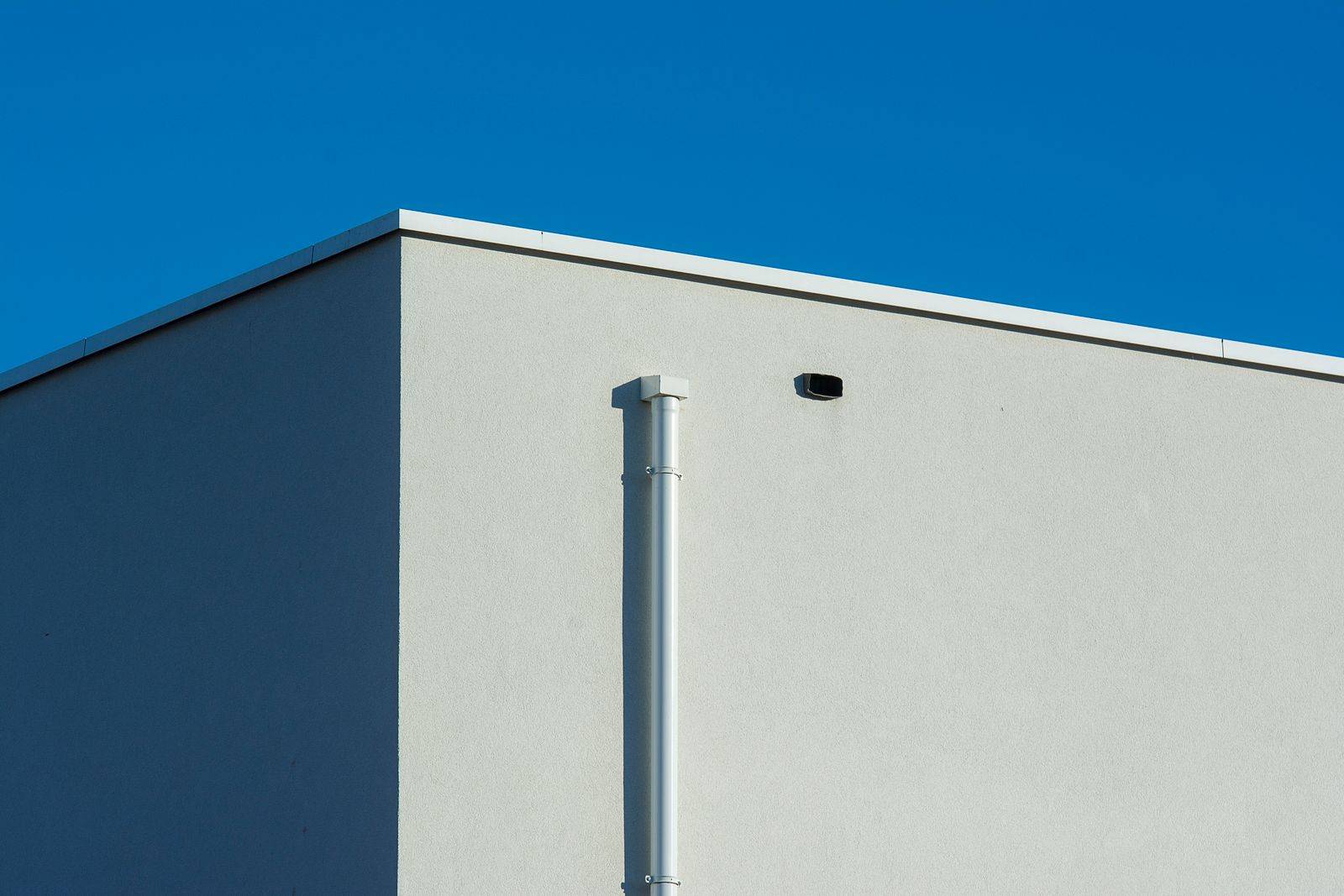 A white downspout running down the corner of a sunlit building against a blue sky