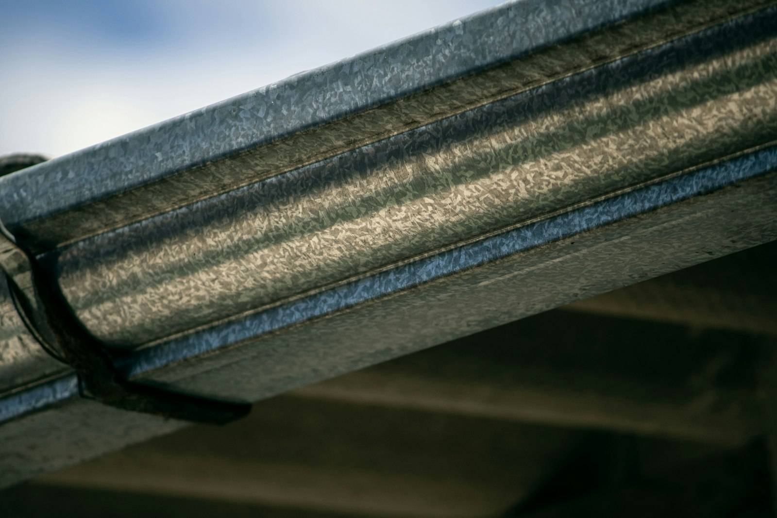 A close-up of a galvanized steel gutter run with a hanger clip