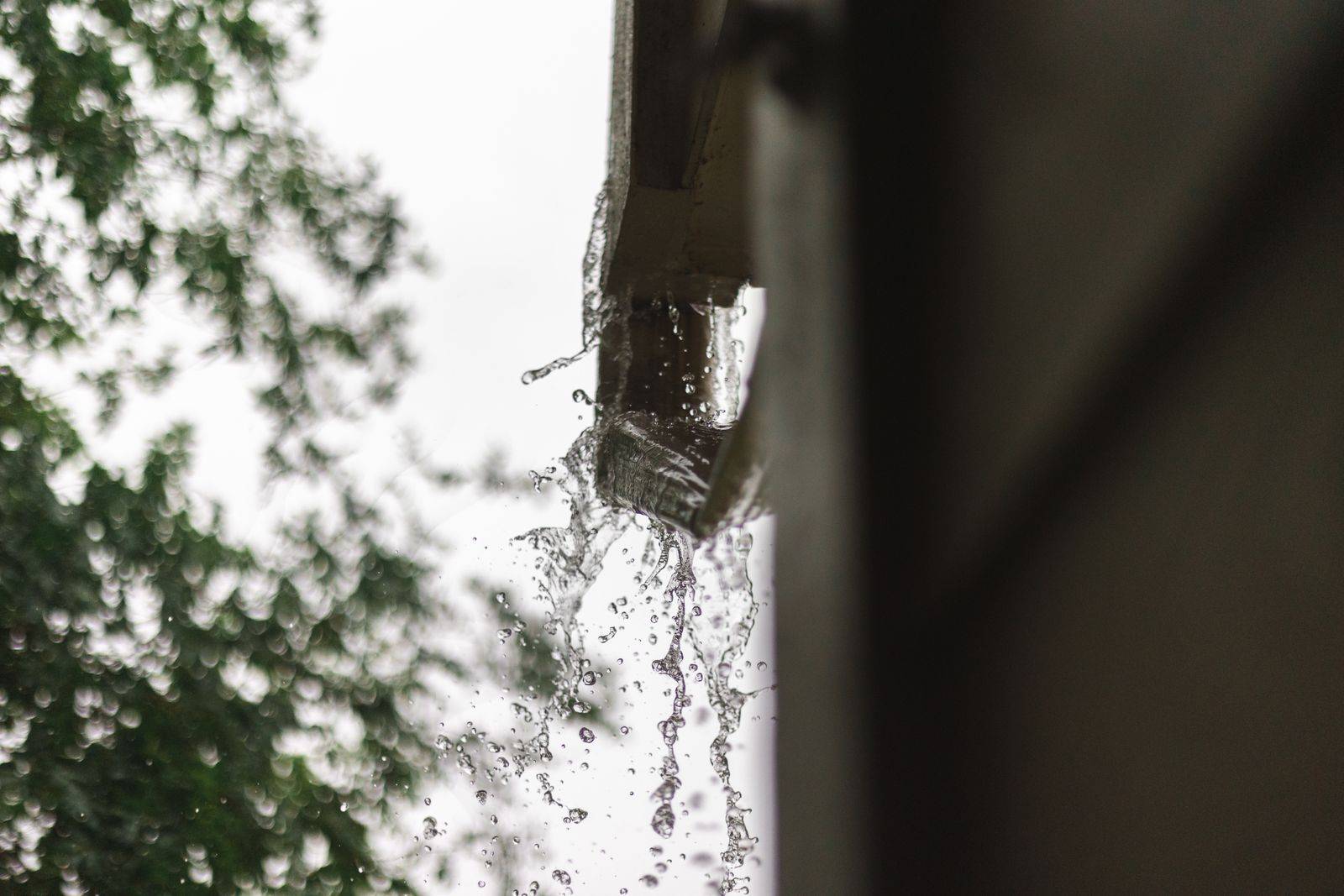 Water spilling dramatically over the front edge of a gutter during rain