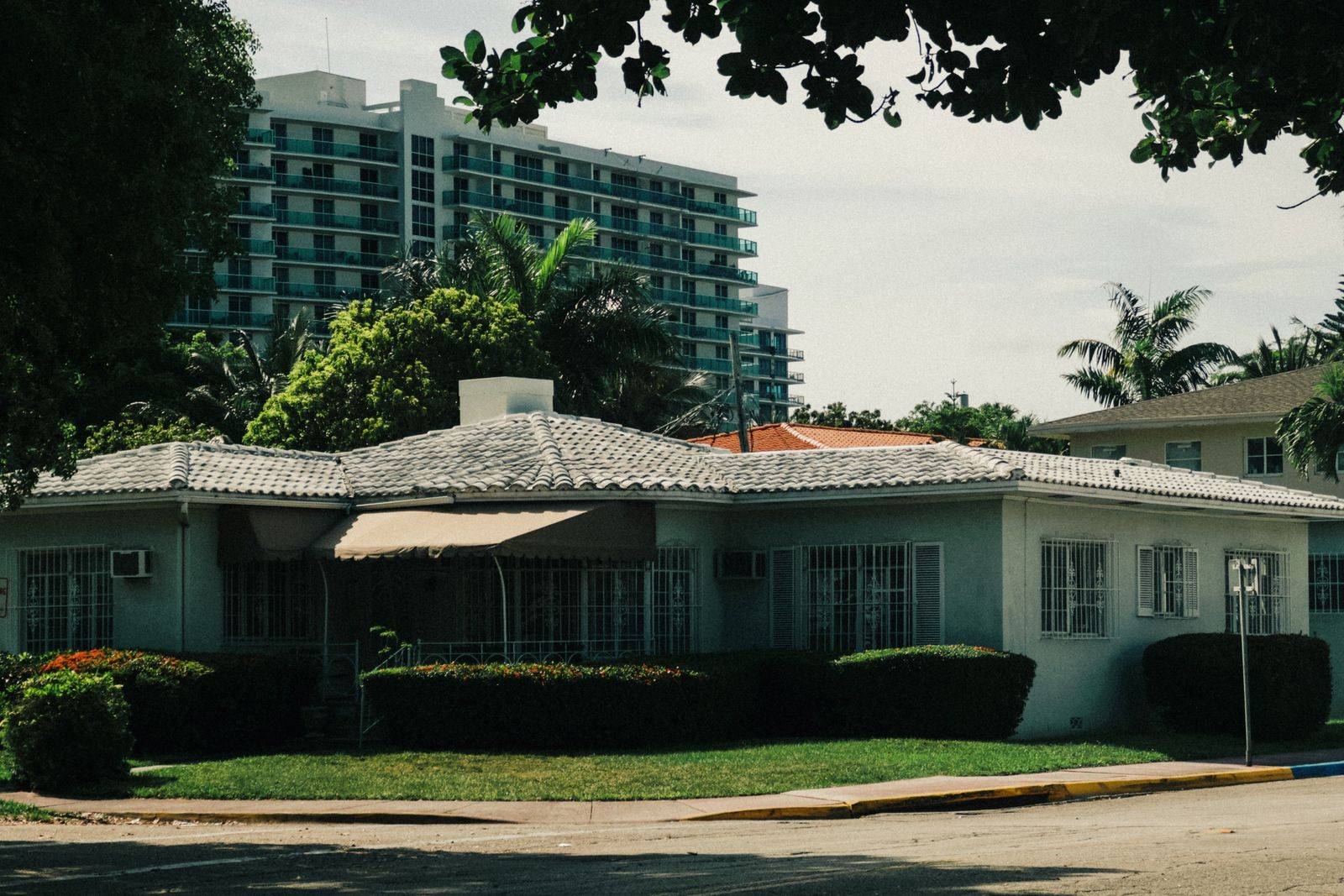 A Miami ranch-style house with barred windows and a condo tower in the background