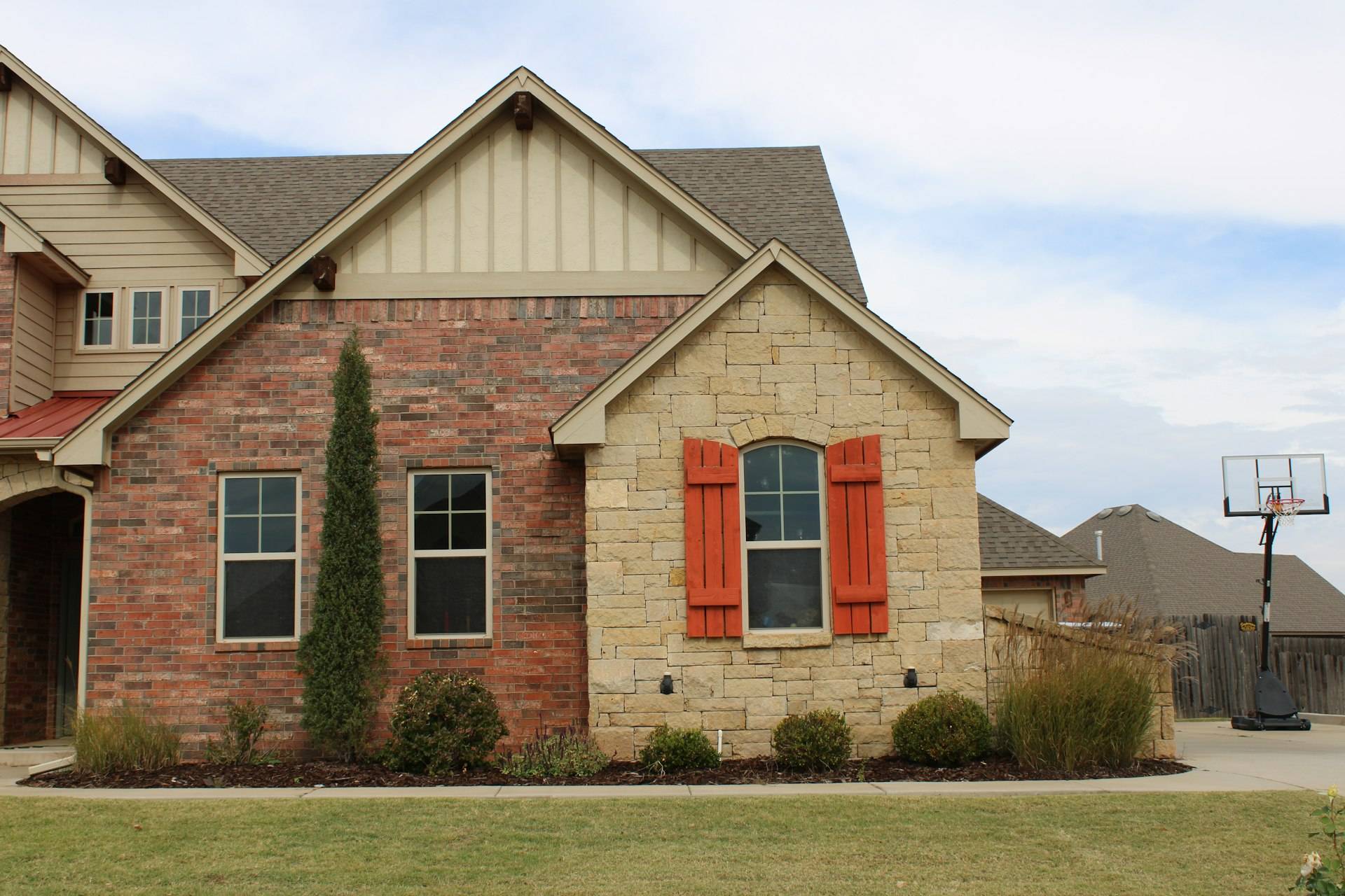A brick and stone house exterior with orange shutters in Oklahoma City