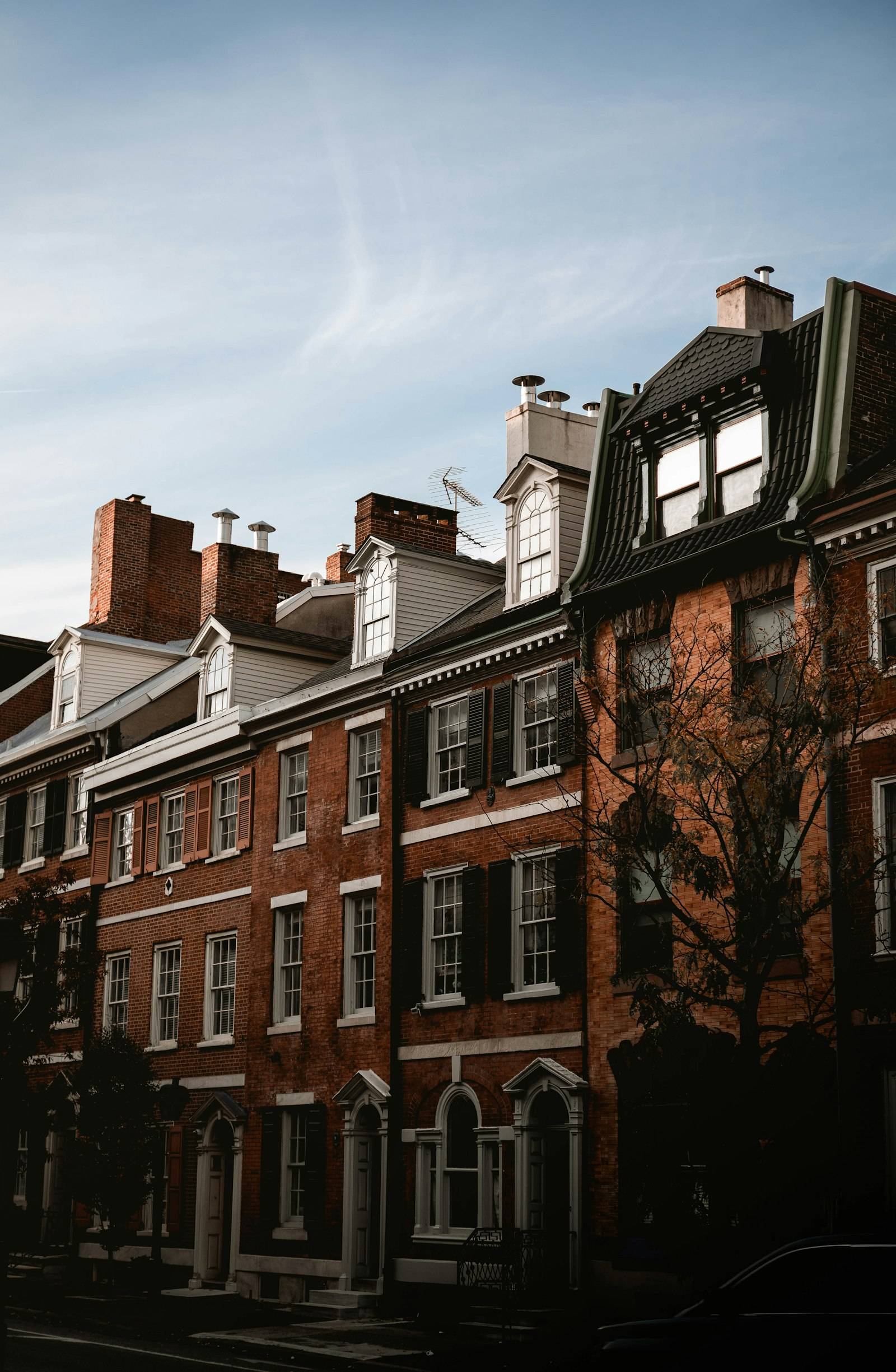 A row of historic brick Philadelphia rowhouses with dormers and chimneys