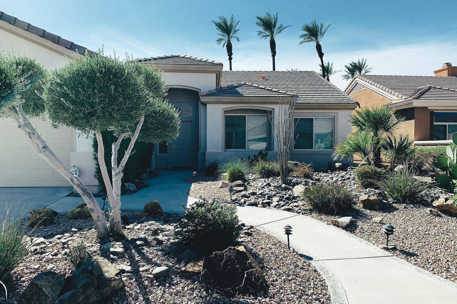 A desert stucco ranch house with xeriscape landscaping, cacti, and palm trees in Phoenix