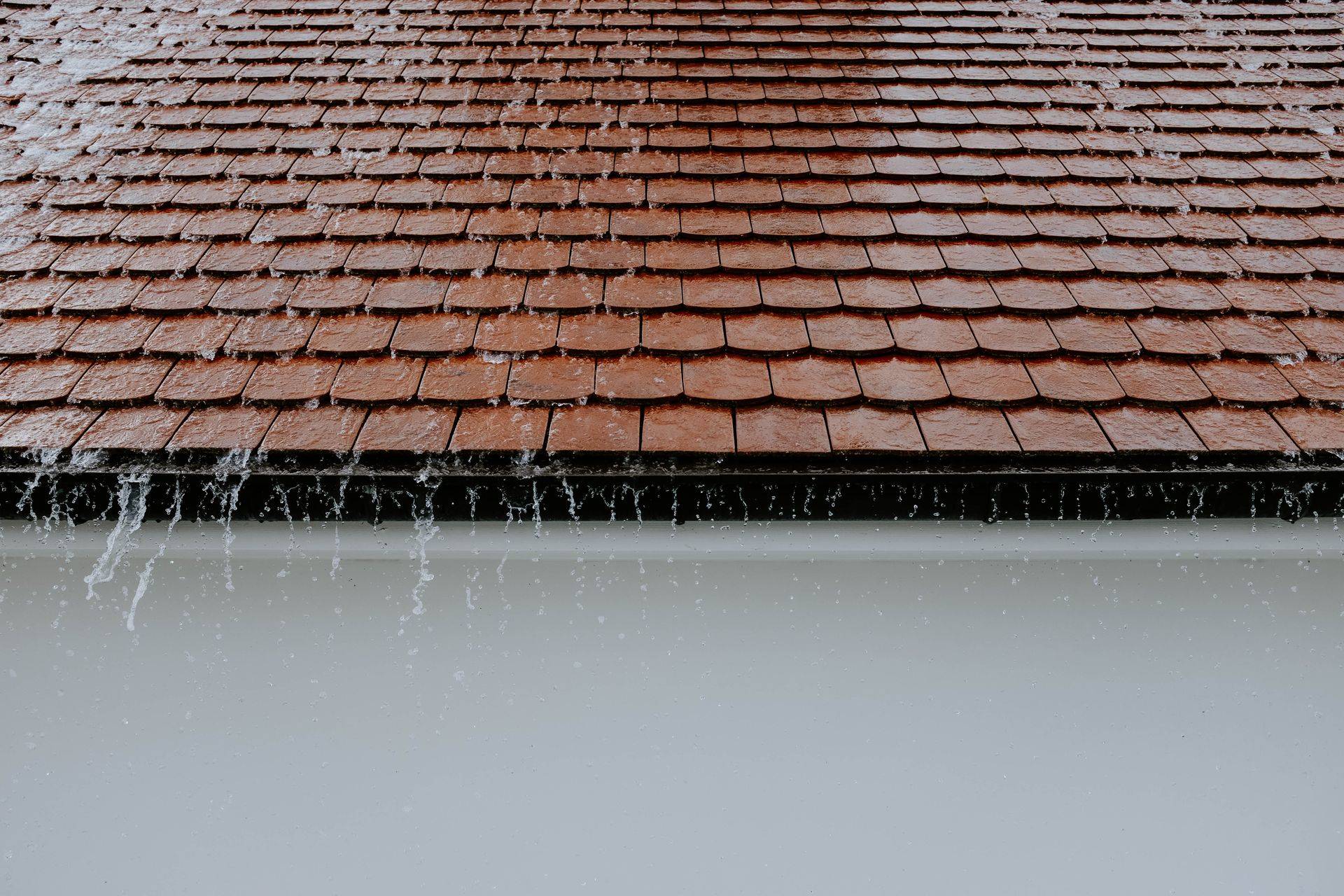 Rain streaming off a tiled roof edge during a heavy downpour