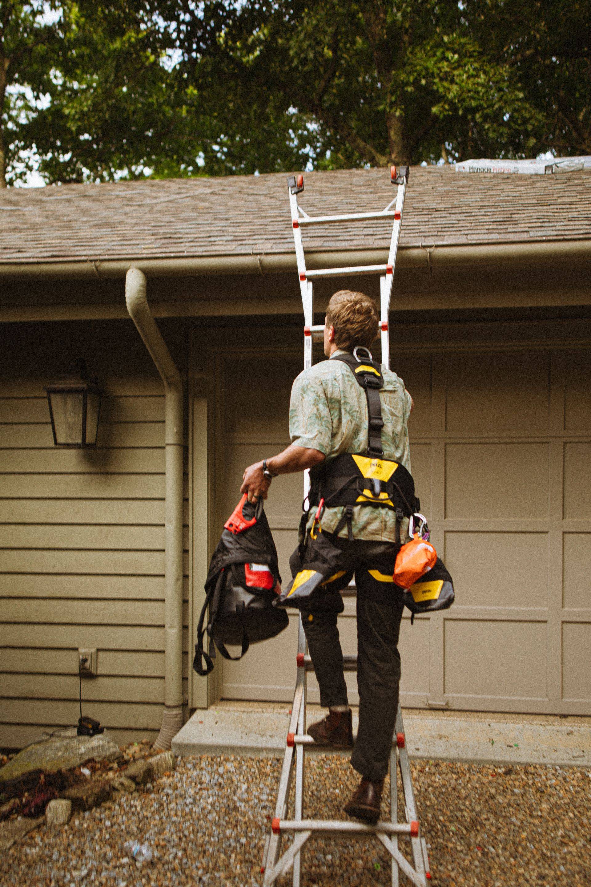 A worker in safety equipment climbing a ladder positioned against a roofline