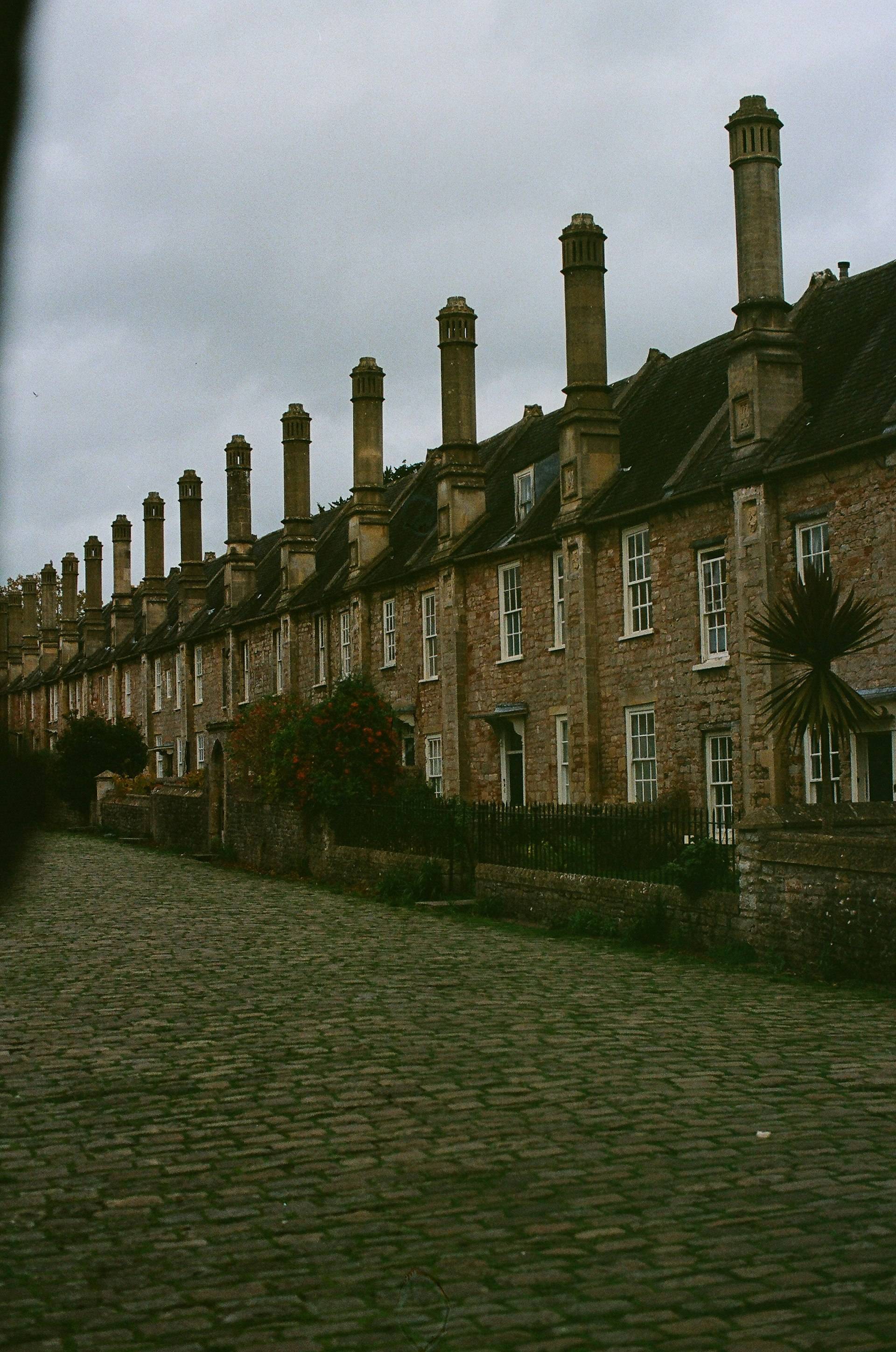 A row of stone cottages with tall chimneys along a cobblestone lane in England