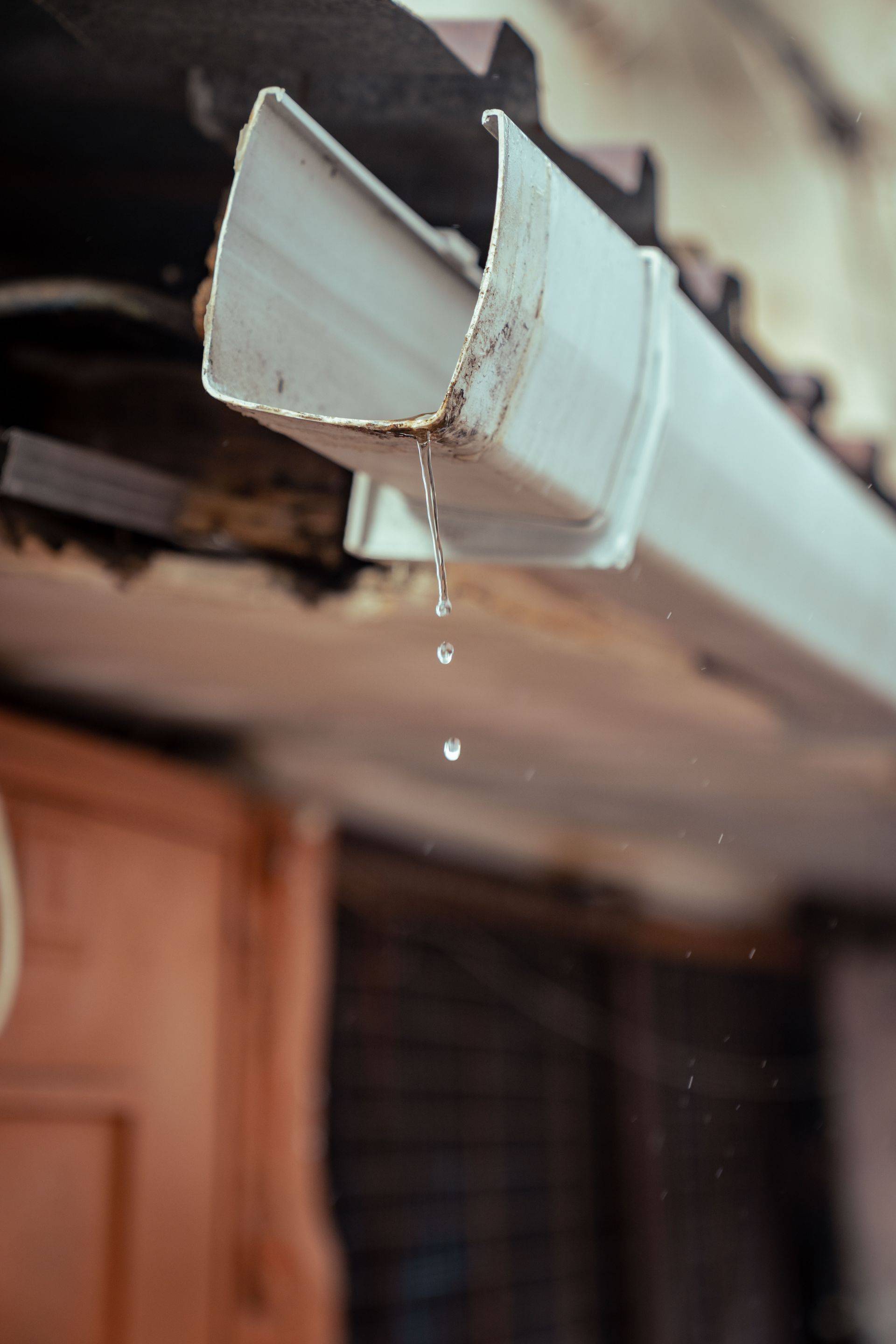 Water droplets collecting and dripping from a metal gutter corner