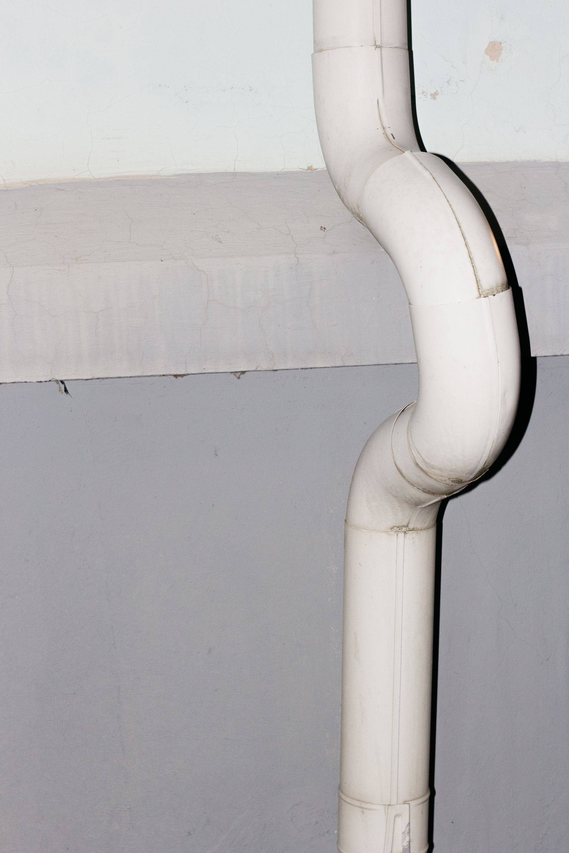 A white downspout with offset joints running down an exterior wall