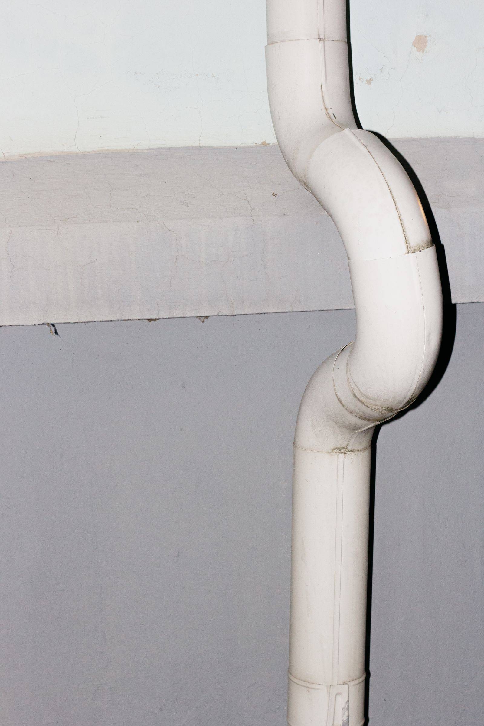 A white vinyl downspout elbow joint against a two-tone wall